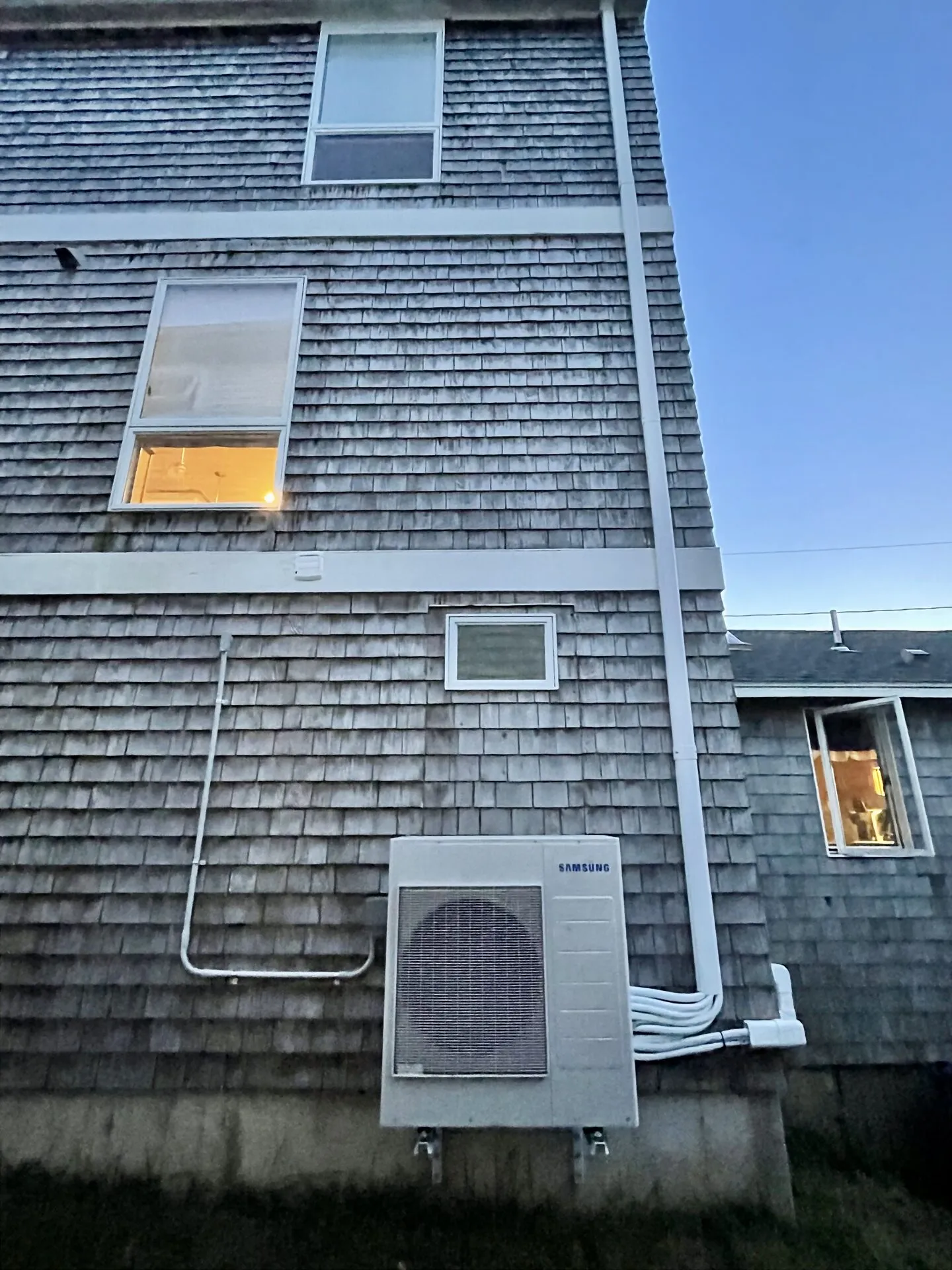 Samsung outdoor heat pump condenser mounted on a cedar-shingled coastal Maine home