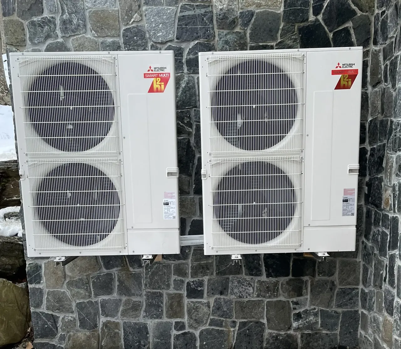Dual Mitsubishi Electric Smart Multi heat pump outdoor units installed on a stone exterior wall in Cape Elizabeth, Maine