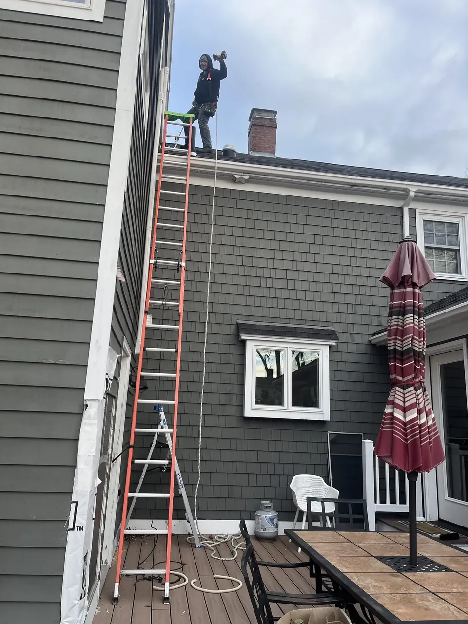 Southern Maine Mechanical technician on a ladder servicing a roofline near the chimney in Southern Maine