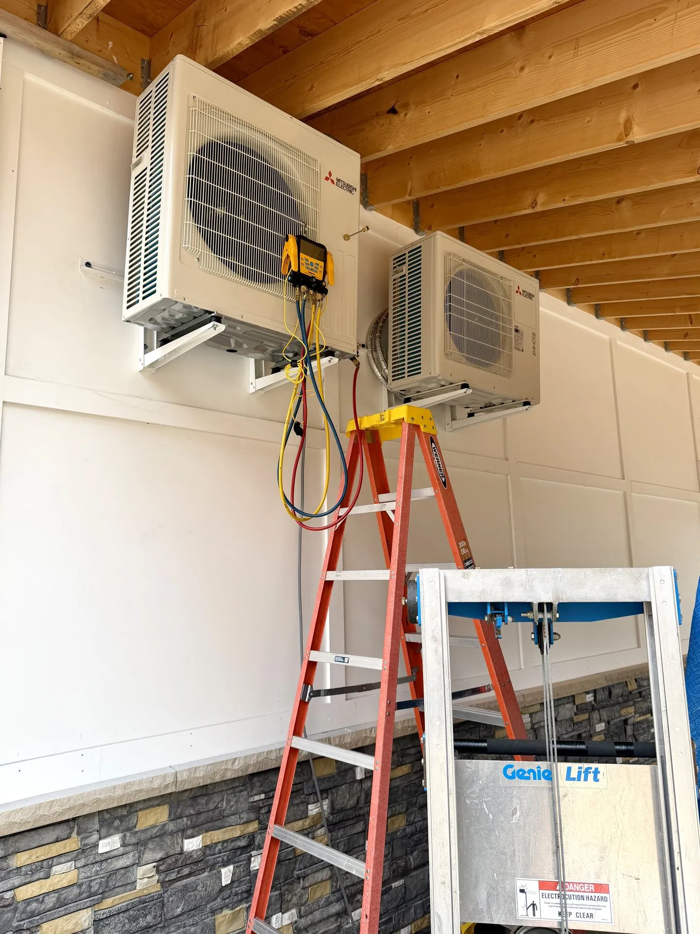 Two Mitsubishi outdoor heat pump units mounted under a deck during a multi-zone install in Southern Maine
