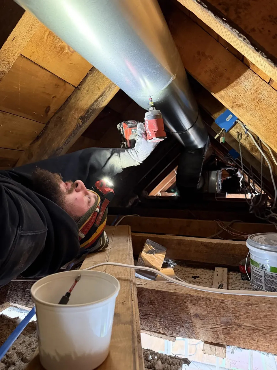 Southern Maine Mechanical technician fastening ductwork in an attic during a heat pump install