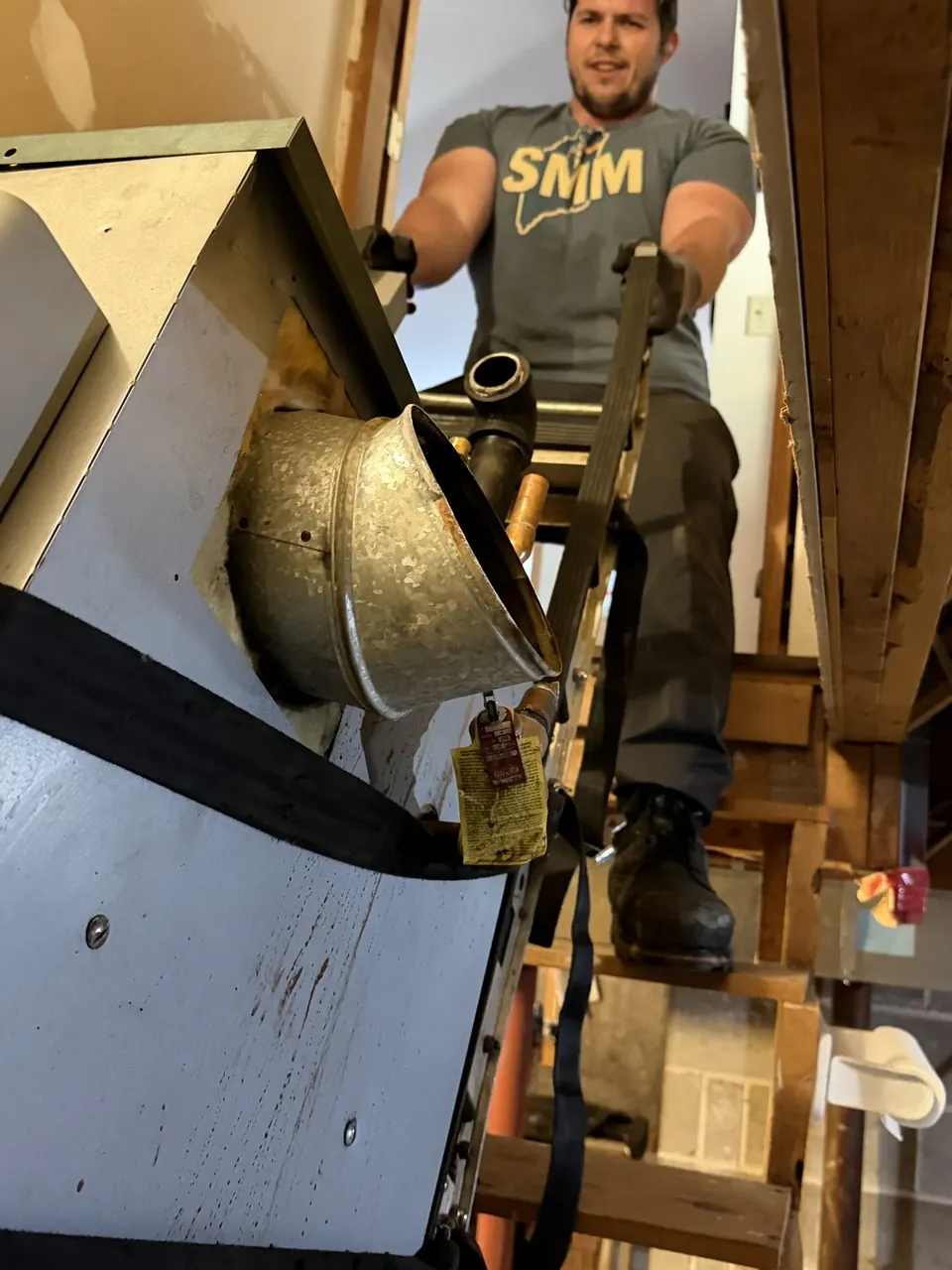 Southern Maine Mechanical technician in an SMM shirt running ductwork from an attic access in Southern Maine